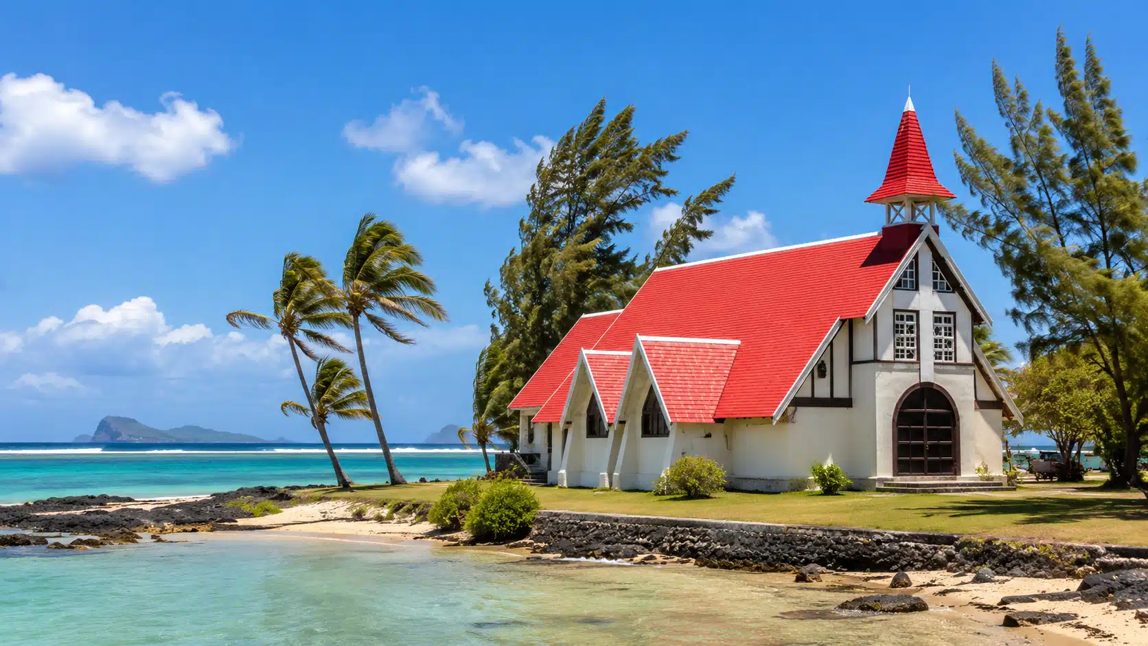 Illustration de la petite chapelle au toit rouge de Cap Malheureux, à l'île Maurice, en bord de lagon turquoise avec des îlots visibles au large.