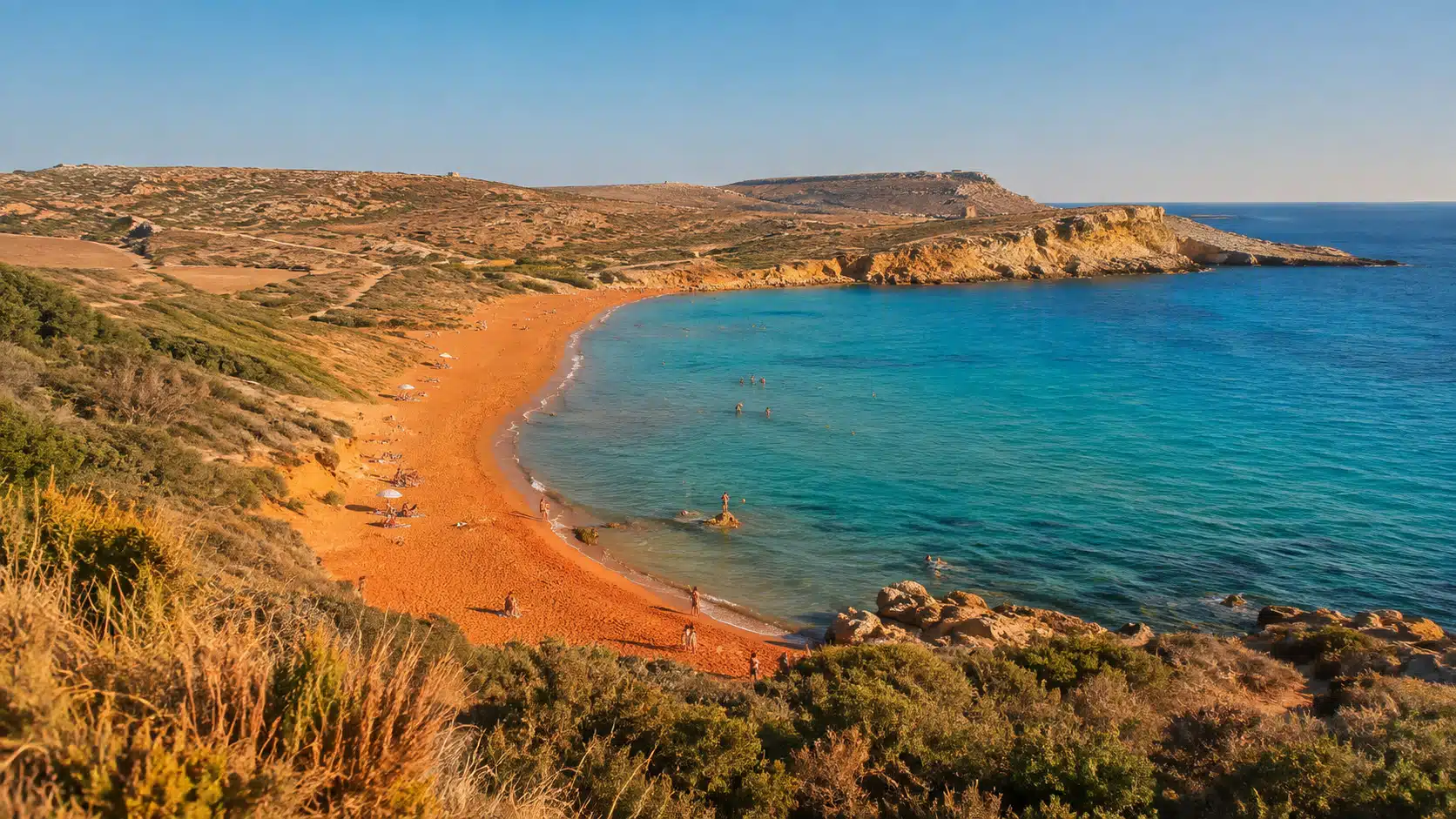 Illustration de la baie de Ramla à Gozo, sable aux reflets rougeâtres bordé de collines arides et d'une eau turquoise.